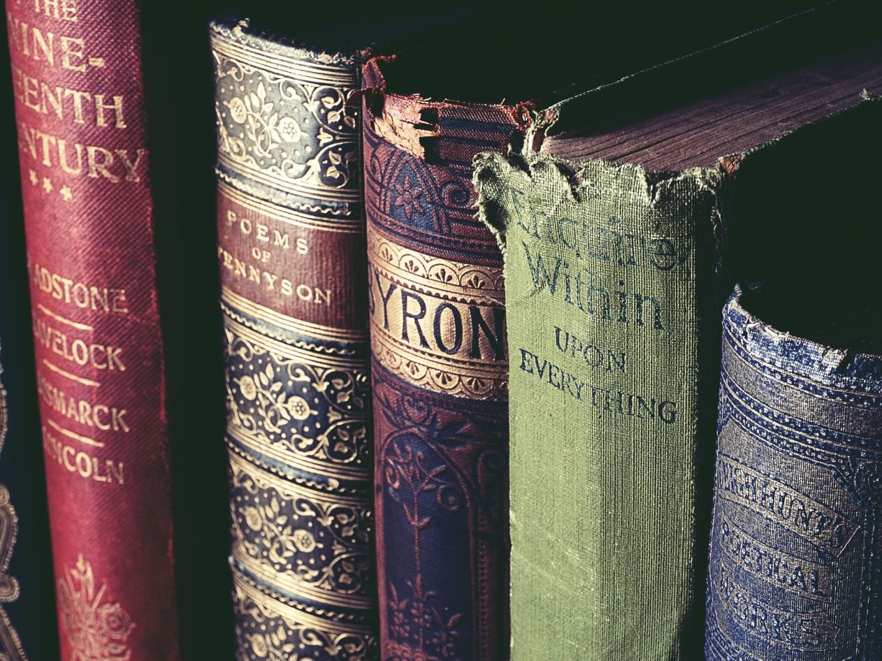 a stack of rare old looking books on a shelf, super close up, showing the spine of the 5 old books.